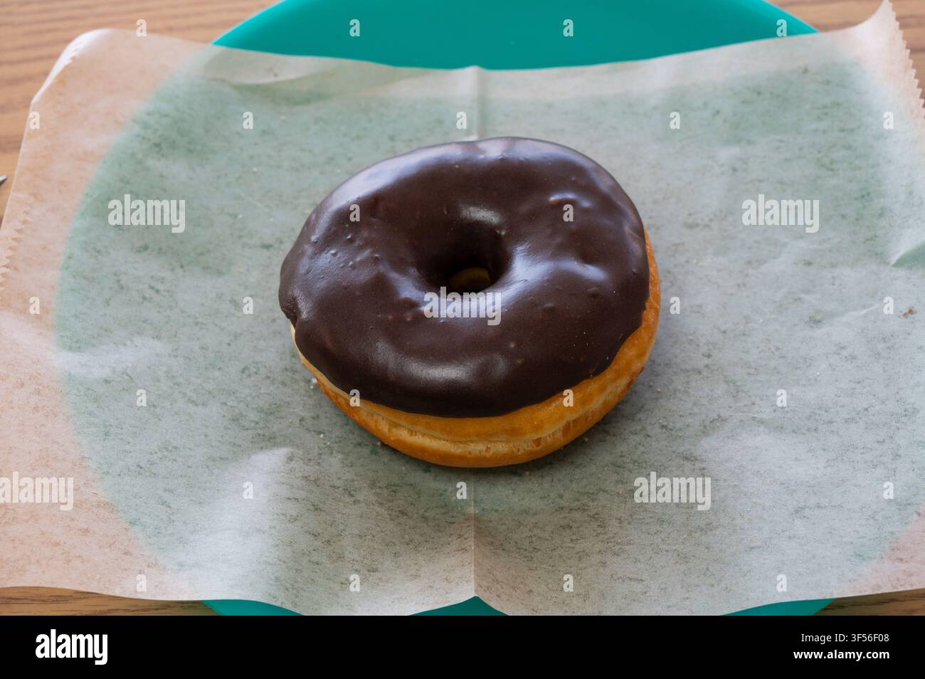 Un donut rotondo con una ricca glassa al cioccolato appoggiato su un foglio di carta cerata su un piatto. Foto Stock