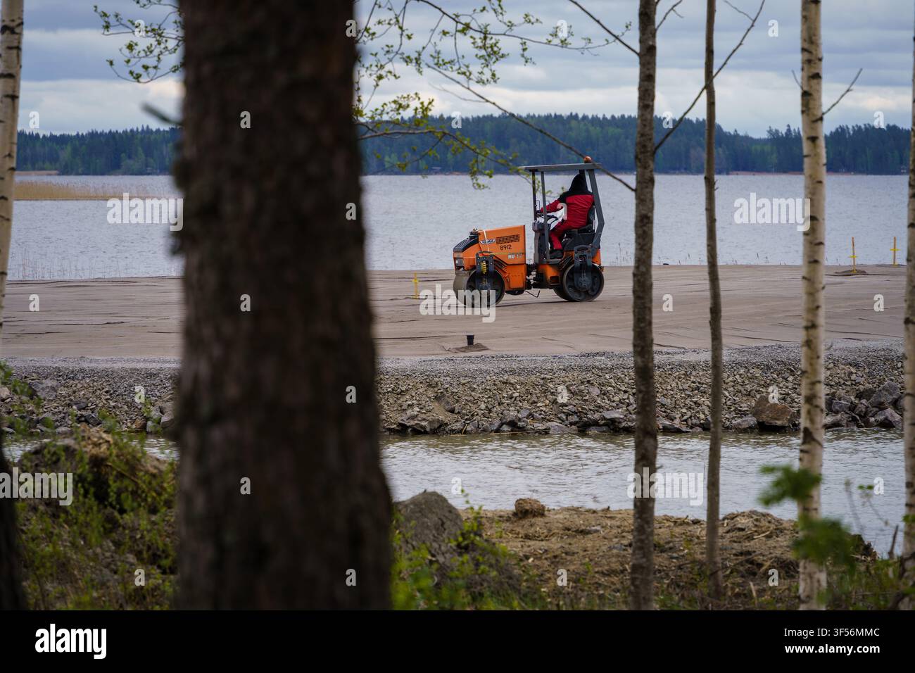 Iitti, Finlandia - 14 maggio 2026 - Lavoratore che aziona un rullo vibrante vicino a un lago Foto Stock