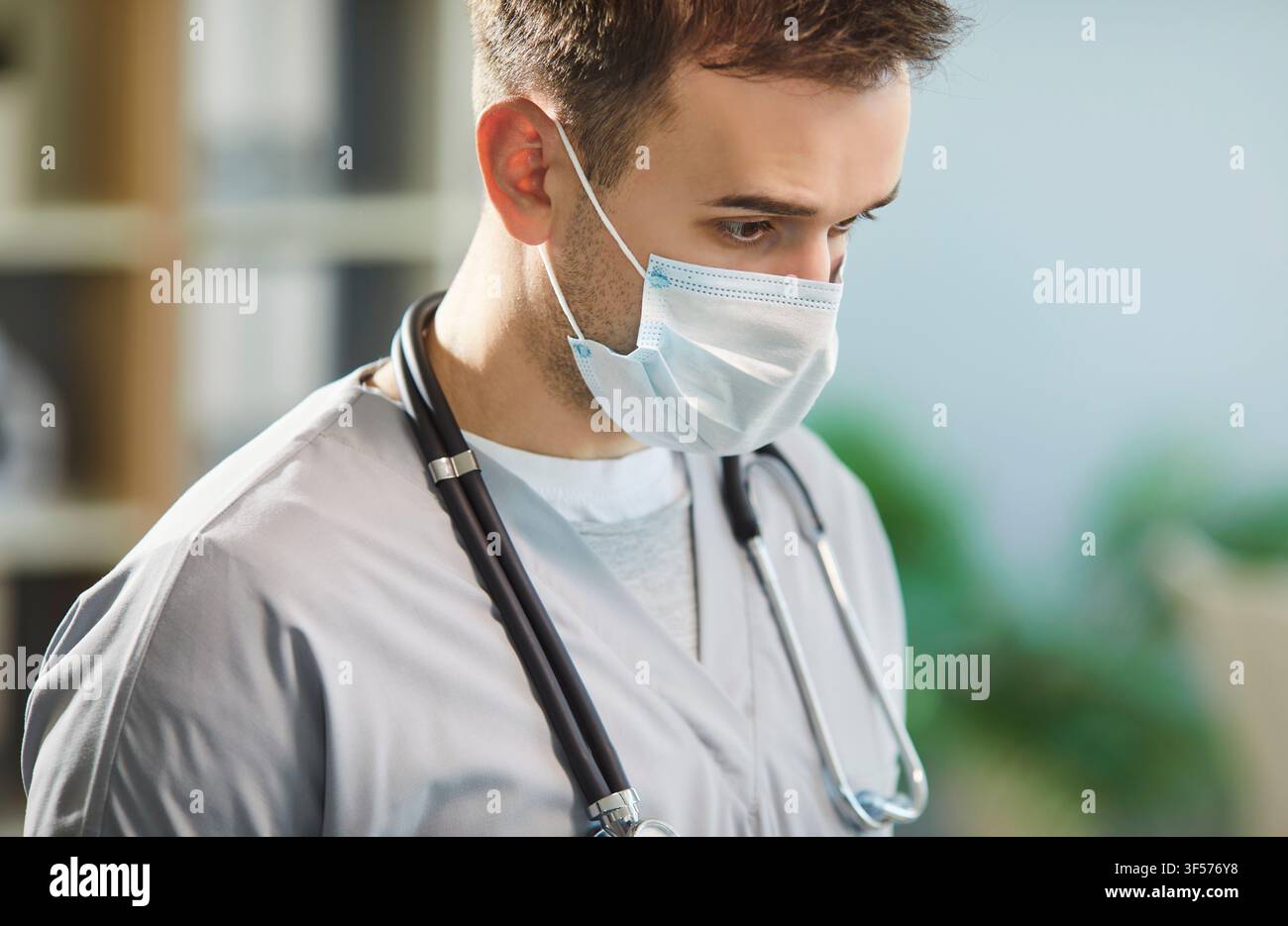 Ritratto ravvicinato di un uomo pensieroso, medico o infermiere, con mascherina blu in piedi in una clinica medica Foto Stock