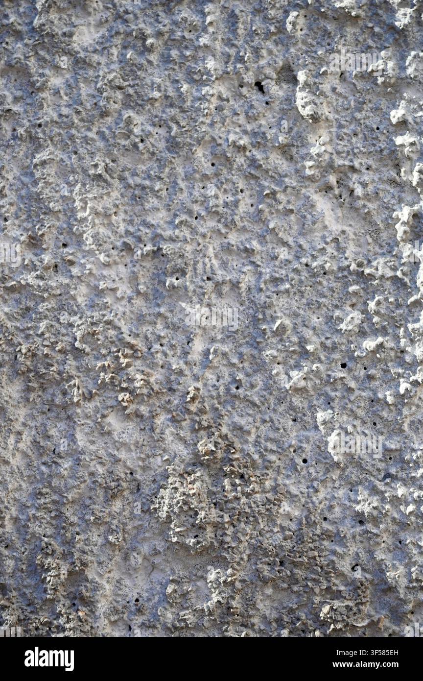 Una fotografia macro verticale dettagliata di una superficie di cemento grigia ruvida e porosa con fosse, zone irregolari e texture minerali consumate. Foto Stock