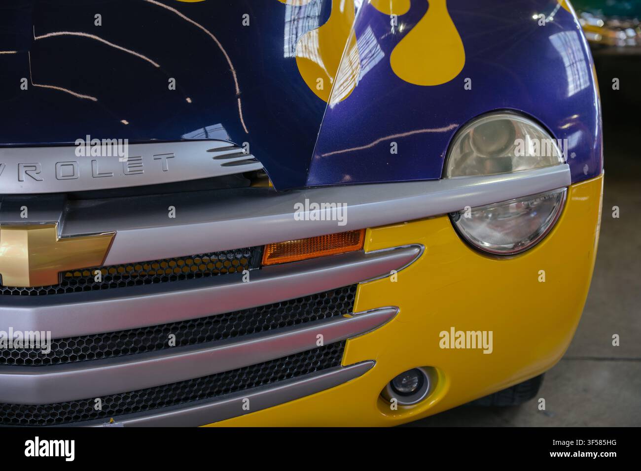 Orlando, FL, USA - 19 marzo 2025: Primo piano della parte anteriore di un'auto personalizzata con faro rotondo, indicatore di direzione arancione e verniciatura colorata blu e gialla. La Foto Stock