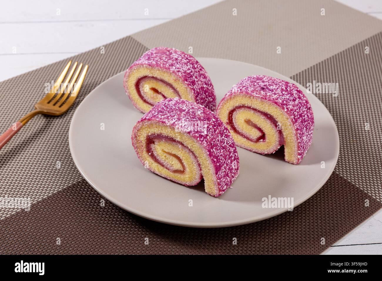 Fette di rotolo di torta di patate dolci viola con fiocchi di cocco e ripieno di marmellata di frutti di bosco su sfondo scuro, dessert gourmet Foto Stock