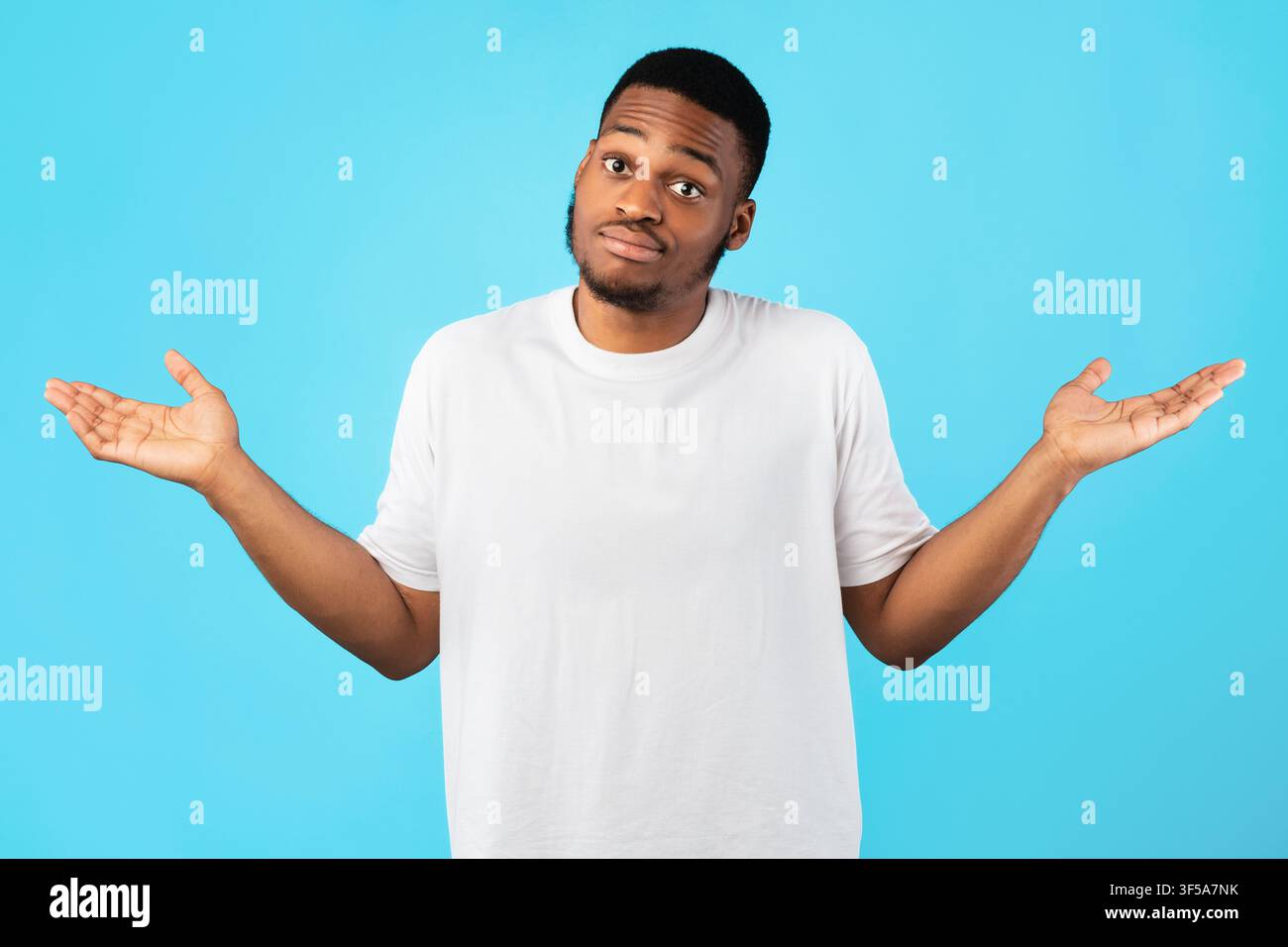 Young Black Man Shrugging spalle in posa su sfondo blu Foto Stock