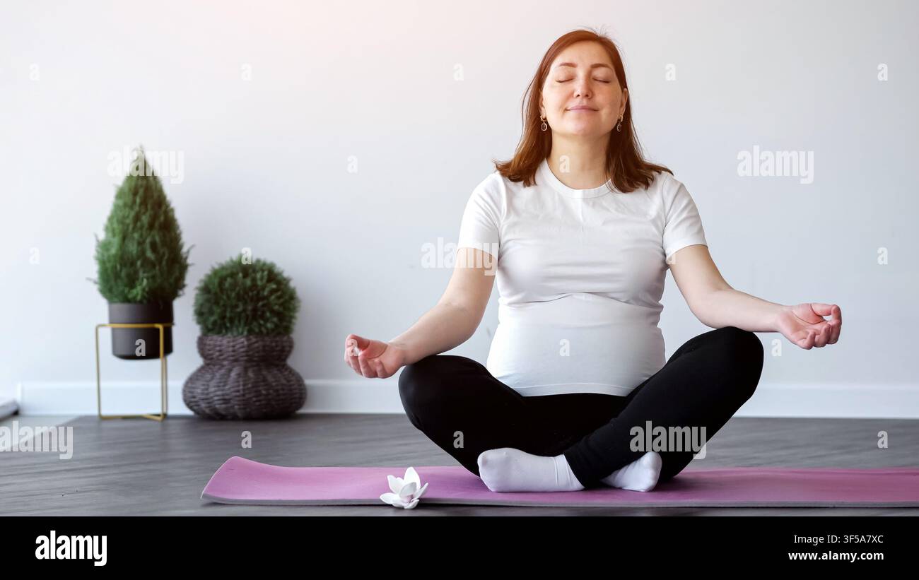 Donna incinta che medita sul tappetino yoga a casa Foto Stock