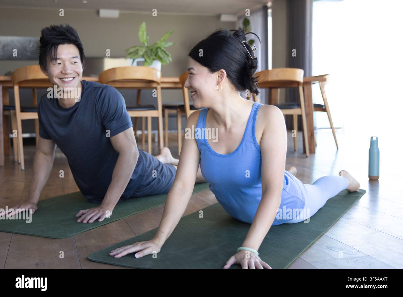 Coppia asiatica in abbigliamento sportivo che pratica yoga su materassini verdi a casa con una bottiglia d'acqua Foto Stock