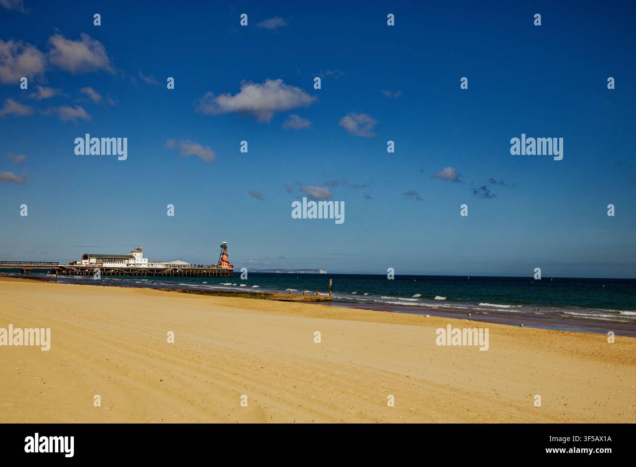 Sabbie dorate su una spiaggia accanto a un mare blu profondo con un molo sullo sfondo, Bournemouth, Dorset, Inghilterra. Foto Stock