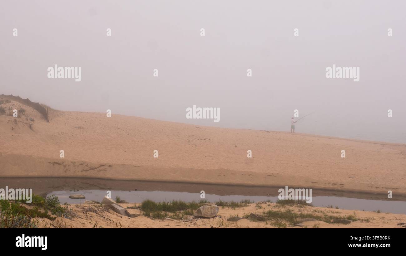 Pescatore solitario che pesca accanto alle dune di sabbia, una scala di legno sepolta e un flusso di marea nella fitta nebbia marina, costa atlantica, Portogallo — Solitudine Foto Stock