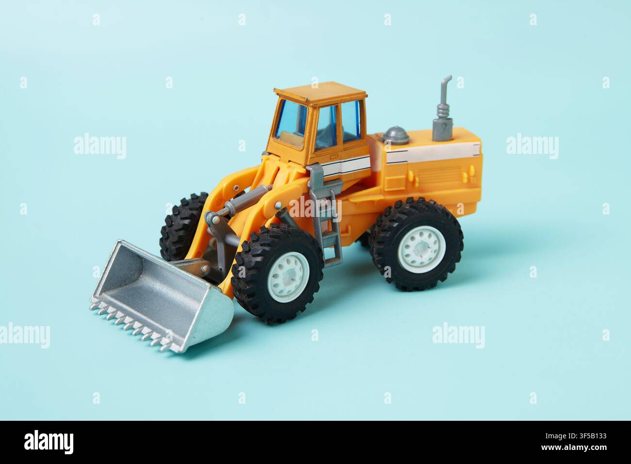 Un realistico giocattolo mini caricatore su ruote su uno sfondo blu morbido. Il modello dettagliato del veicolo da cantiere presenta una benna anteriore sollevata Foto Stock