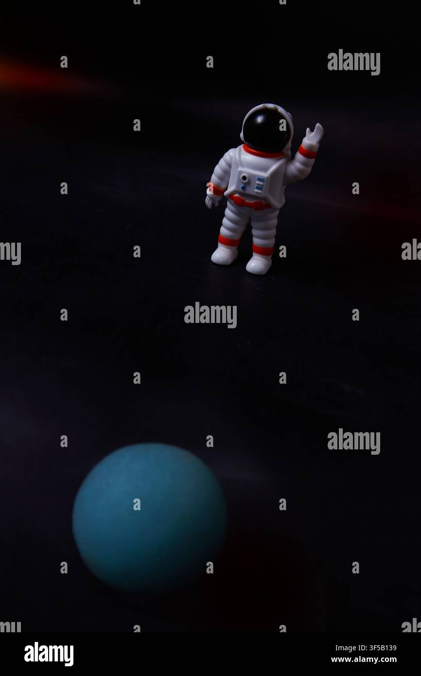 Un astronauta in miniatura sembra fluttuare nello spazio profondo sopra un pianeta blu luminoso Foto Stock