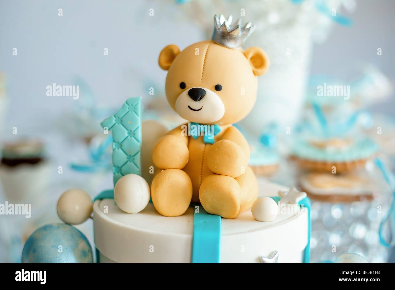 Topper per primo compleanno con un simpatico orso in pasta di zucchero che indossa una corona d'argento. Palette di colori blu e bianchi, decorazione per compleanno di un bambino, topper per torta personalizzato e dessert per feste Foto Stock