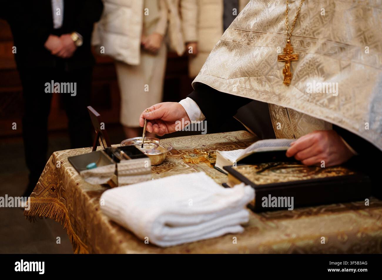 Cerimonia religiosa con un sacerdote che benedice l'acqua santa accanto a un libro sacro e un asciugamano bianco sull'altare. La scena riflette la tradizione sacra, la preghiera e il rituale spirituale Foto Stock