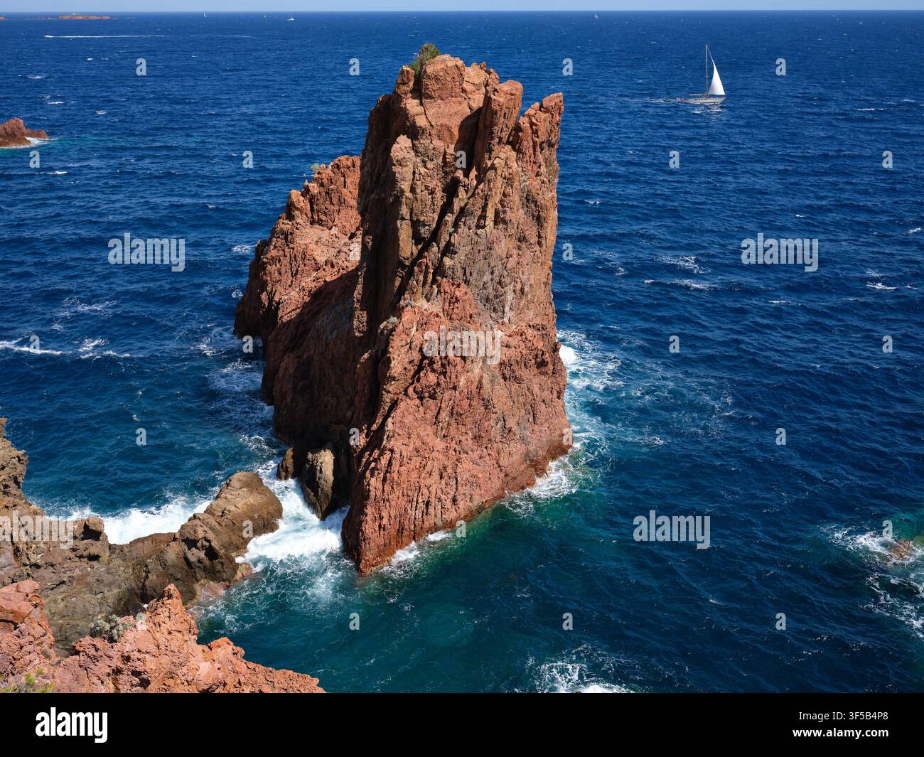 Una barca a vela naviga vicino a uno spettacolare pilastro di mare rosso al largo del massiccio dell'Esterel, sulle rive del Mediterraneo. Saint-Raphaël, Var, Francia. Foto Stock