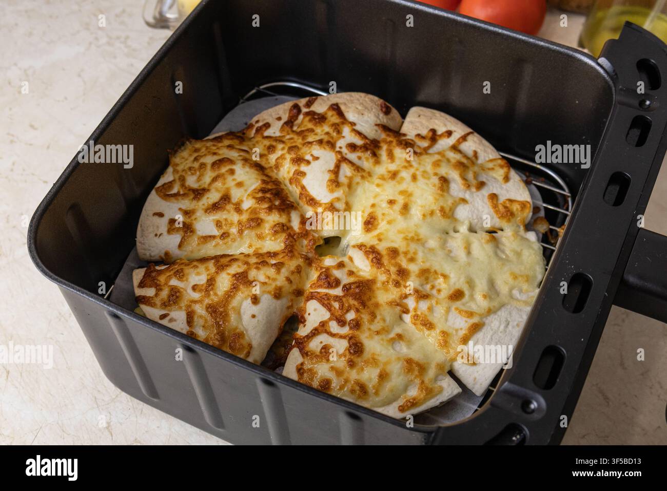 Un piano orizzontale dall'alto che mostra wedge di quesadilla con tortilla al formaggio fuso dorato, cotte alla perfezione all'interno di un cestello di friggitrice ad aria elettrica nero Foto Stock