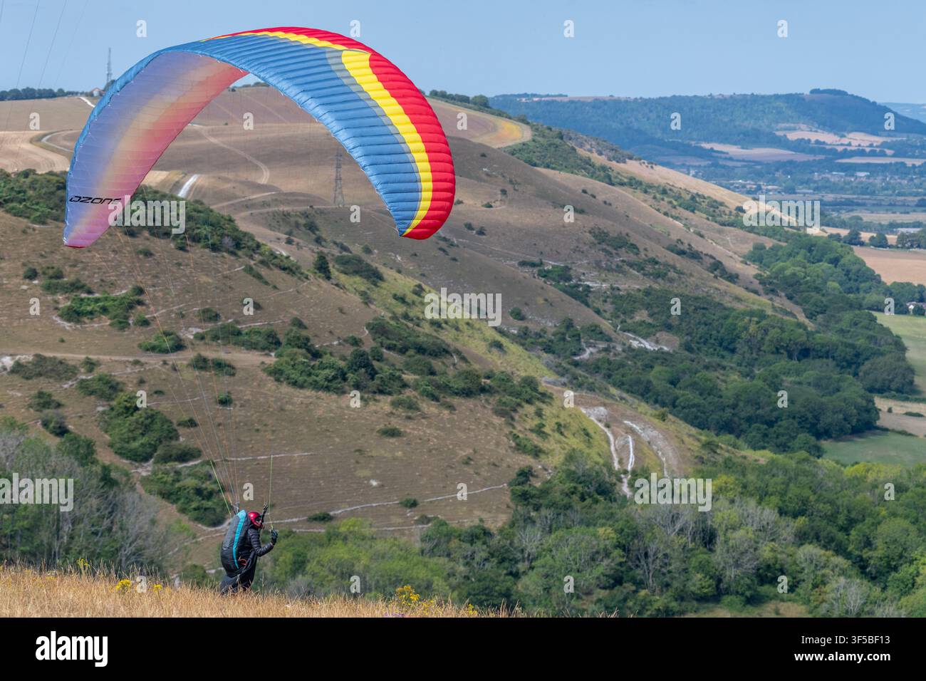 Brighton, 31 luglio 2026: Un parapendite sul punto di decollare a Devil's Dyke, appena a nord di Brighton, per un volo sopra i South Downs nazionali arsi dal sole Foto Stock