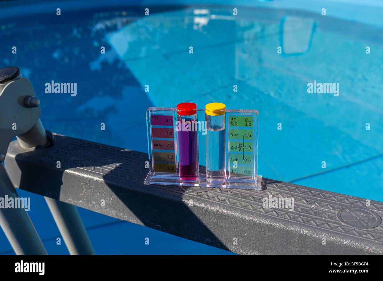 Una vista prospettica orizzontale di un kit per il test della qualità dell'acqua chimica con liquidi reagenti viola e gialli appoggiati sul bordo di una piscina con telaio a Bri Foto Stock