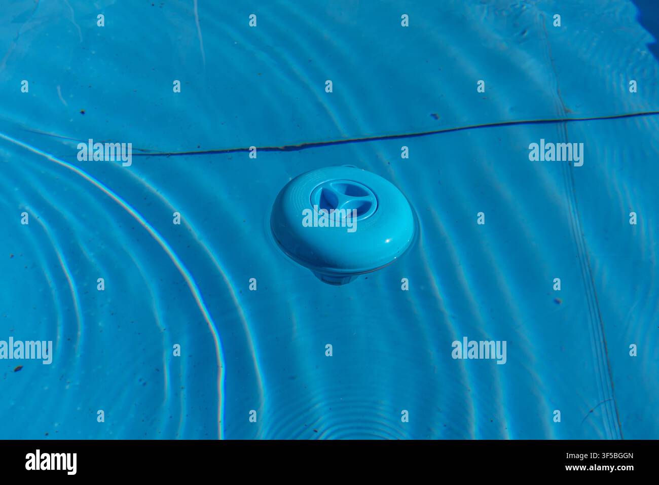 Un primo piano orizzontale di un distributore di cloro galleggiante in plastica blu che galleggia sulla superficie dell'acqua pulita e increspata di una piscina blu. Foto Stock