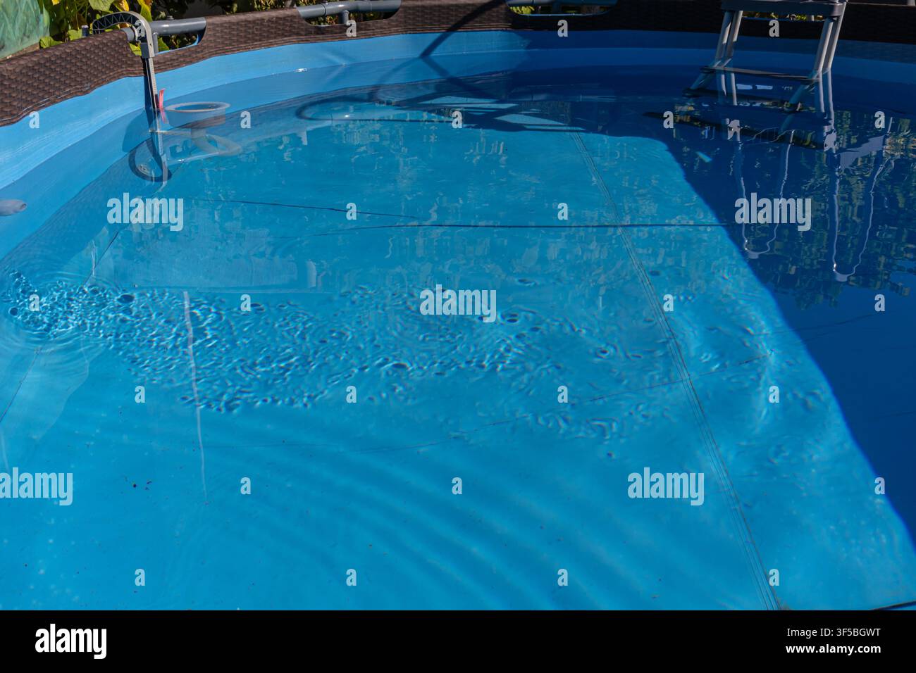 Una fotografia orizzontale ad angolo alto che mostra l'acqua blu trasparente e il fondo blu del liner di una piscina a bordo giardino dopo un trattamento chimico adeguato Foto Stock