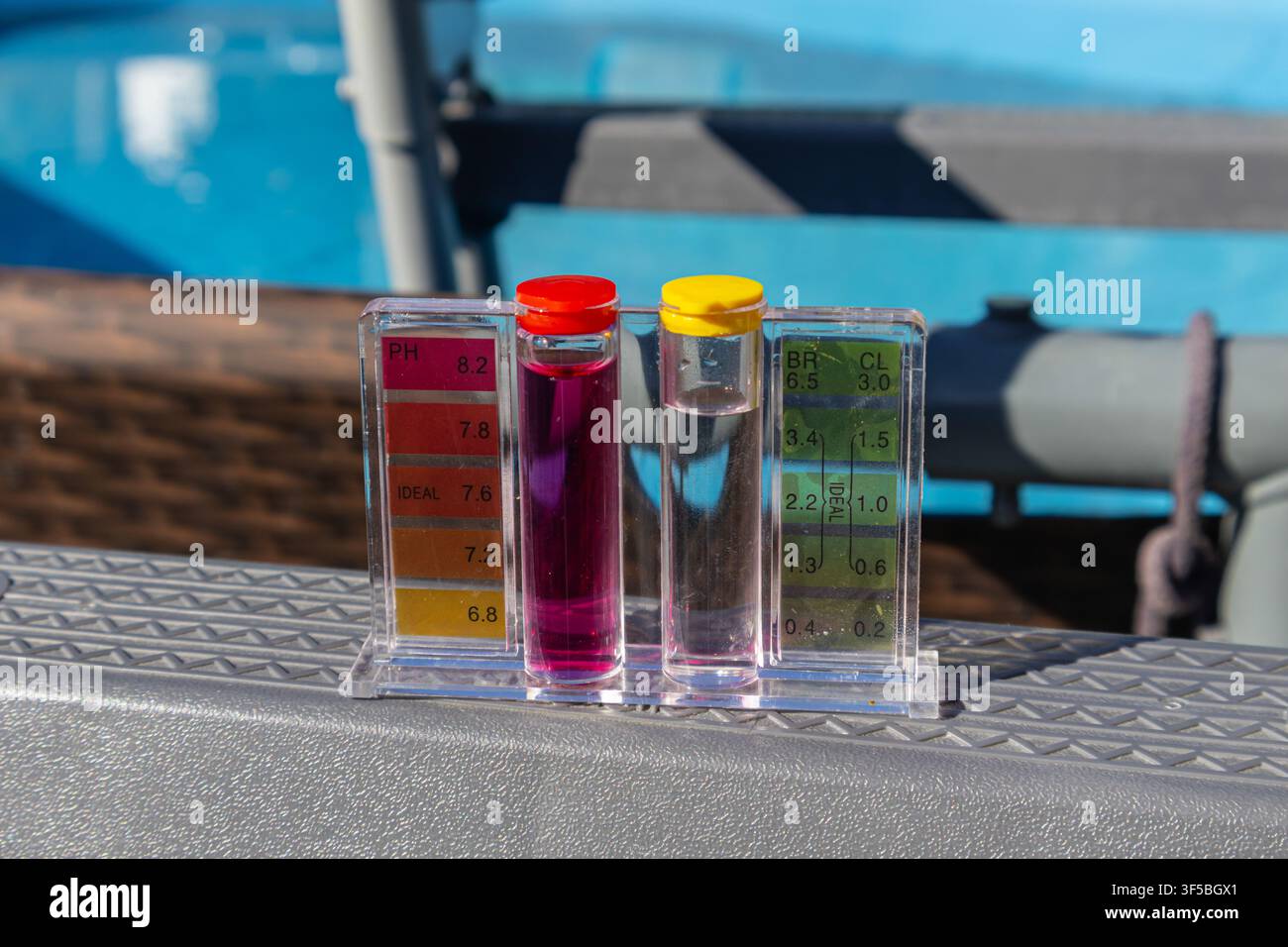 Un'immagine orizzontale all'aperto che mostra un kit comparatore per i test del pH e del cloro dell'acqua in piedi sul bordo grigio della cornice di una pulita piscina blu nel cortile Foto Stock