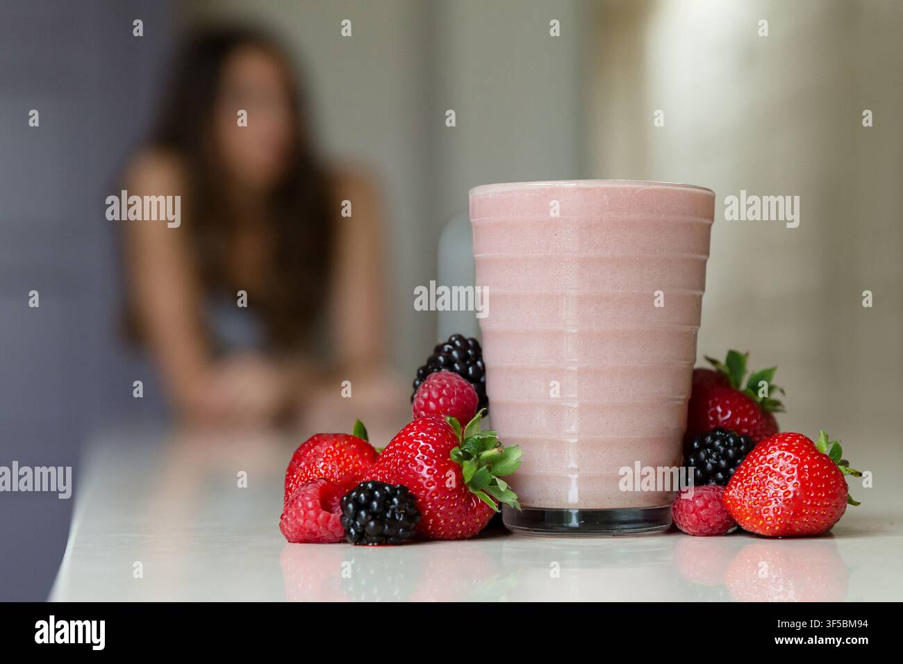 Un frullato di bacche e bacche fresche miste sono disposti in primo piano con una donna fuori fuoco sullo sfondo l'11 giugno 2016. Foto Stock