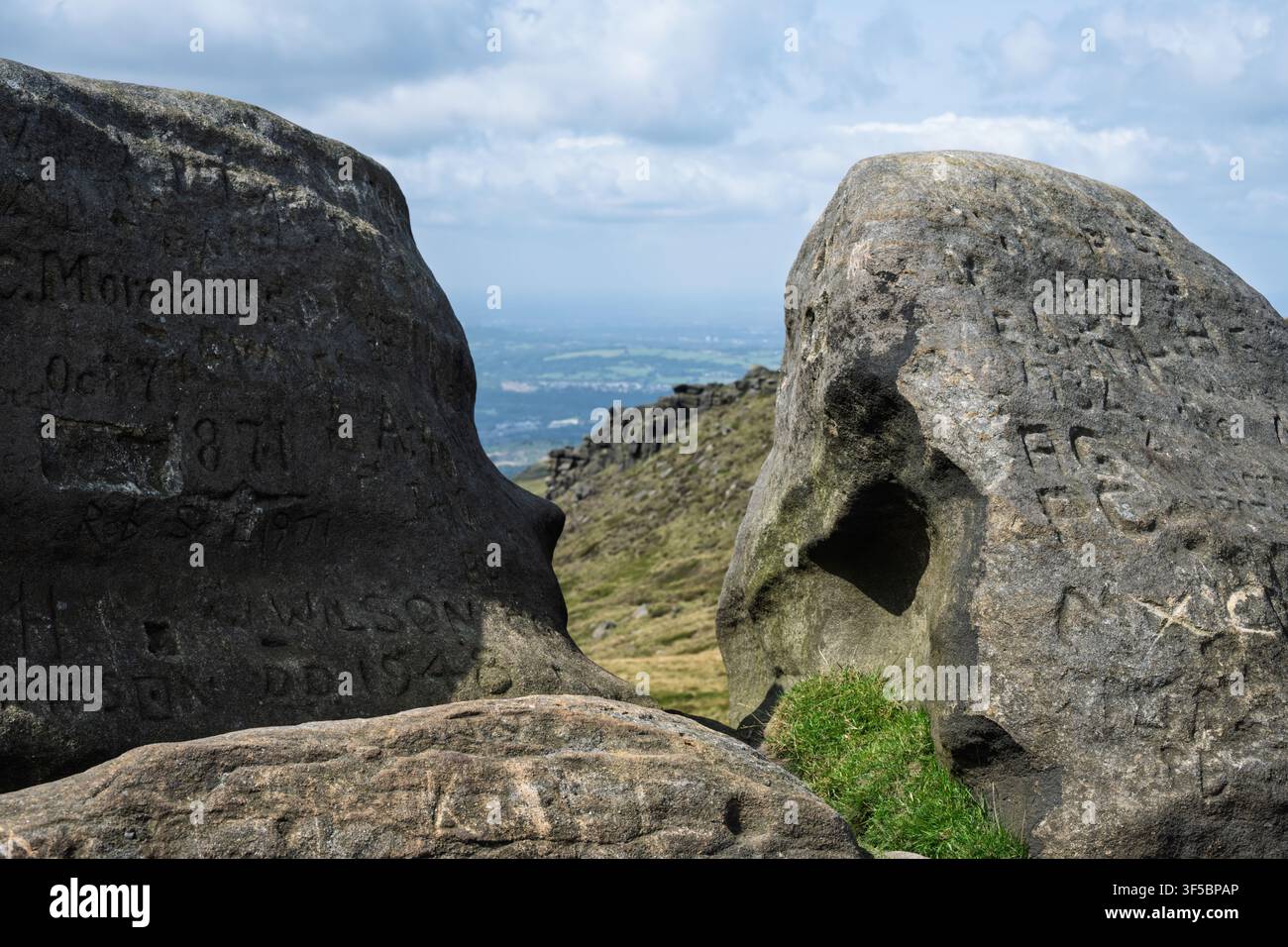 Iniziali e date storiche incise in massi di arenaria erosa incorniciano una vista panoramica distante sulla valle a Higher Shelf Stones, nel Peak District Foto Stock