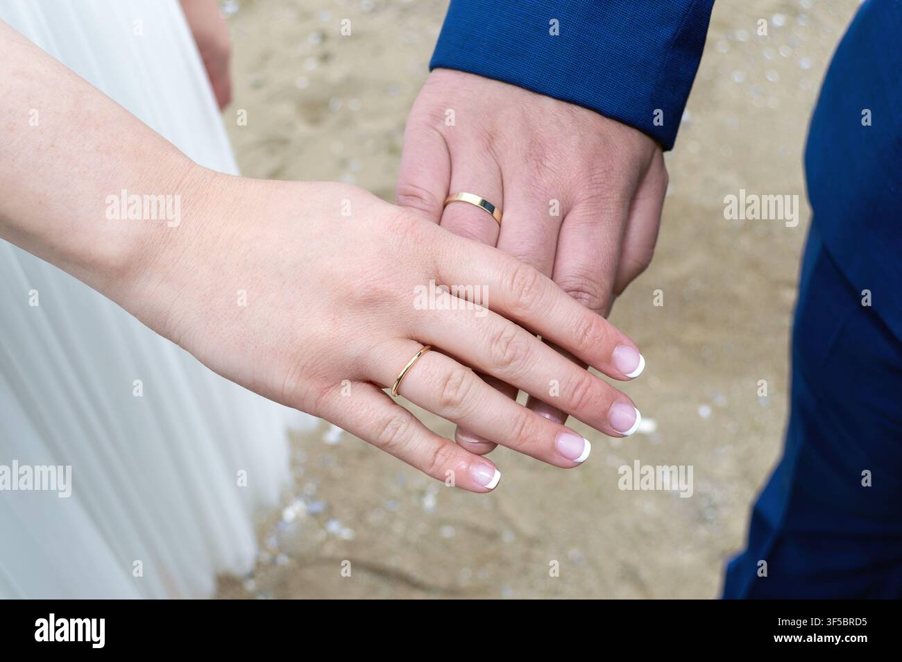 Primo piano di due mani con fedi nuziali che si toccano. Messa a fuoco su dita e anelli d'oro con sfondo morbido. Adatto per temi come il matrimonio Foto Stock
