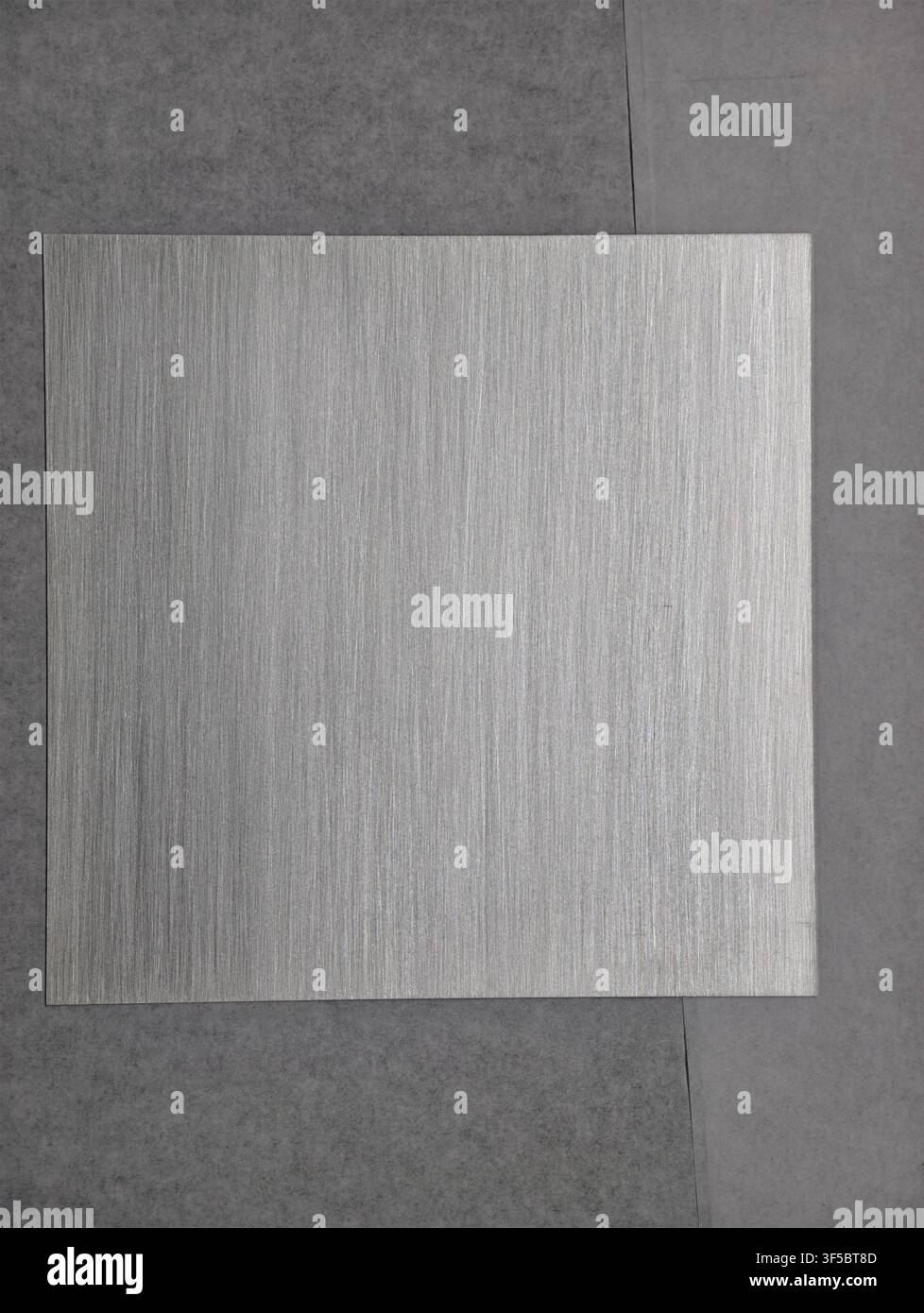 Visualizzazione statica di un foglio metallico sul pavimento indoor, con foglio metallico, da una prospettiva dall’alto, con accenti grigi, argentei e un’atmosfera neutra, che mostra Foto Stock