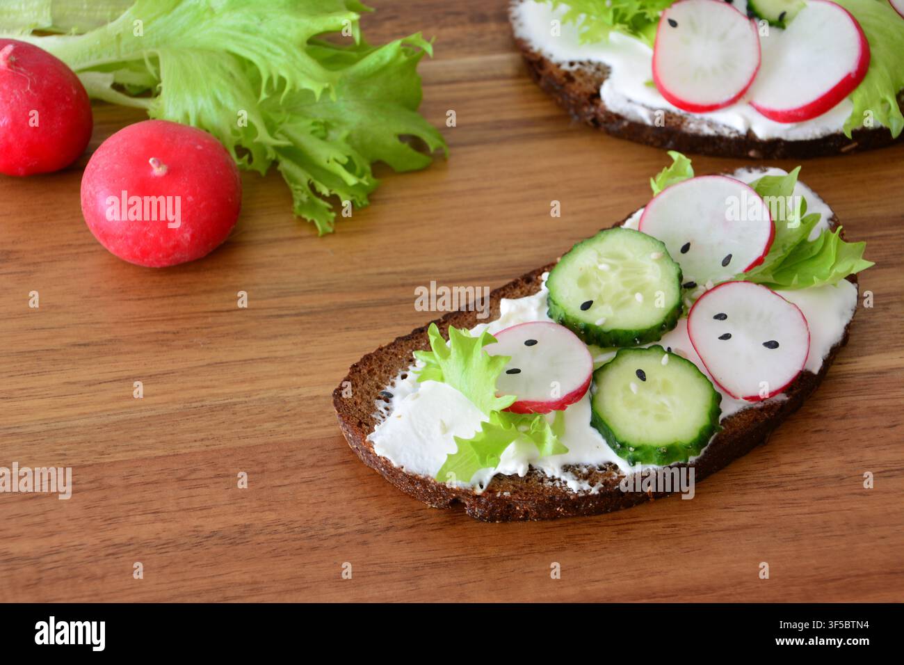 Panini aperti con formaggio fresco, ravanello e cetriolo su una tavola di legno Foto Stock