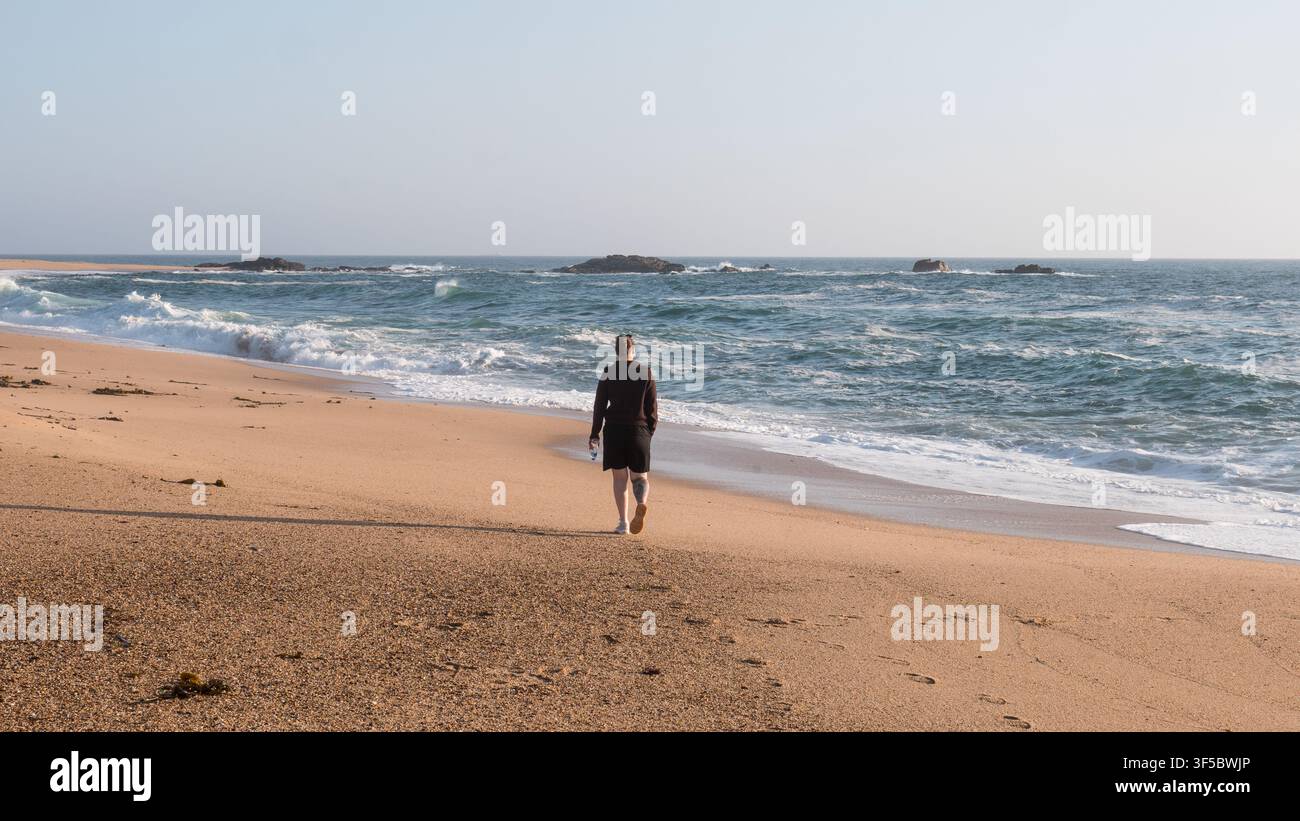 Donna solitaria che cammina verso le onde su una spiaggia atlantica deserta all'alba, nord del Portogallo — Concetto: Solitudine e riflessione, fuga benessere Foto Stock