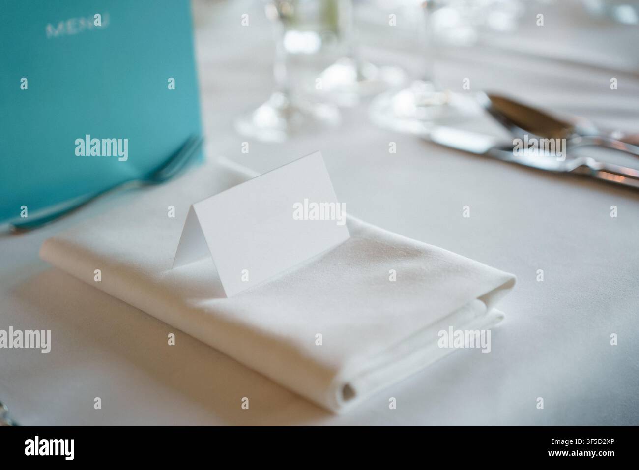 Biglietto da posto bianco vuoto piegato su un tovagliolo ordinatamente piegato, apparecchiatura per una ricevimento di nozze o una cena formale di banchetto, elegante preparazione del banchetto Foto Stock
