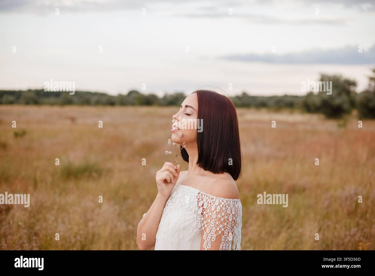 Giovane donna in un abito di pizzo bianco in un prato tranquillo, catturando un momento di pace, connessione con la natura e vibrazioni estetiche delicate, serenità e consapevolezza, connessione pacifica all'aperto Foto Stock