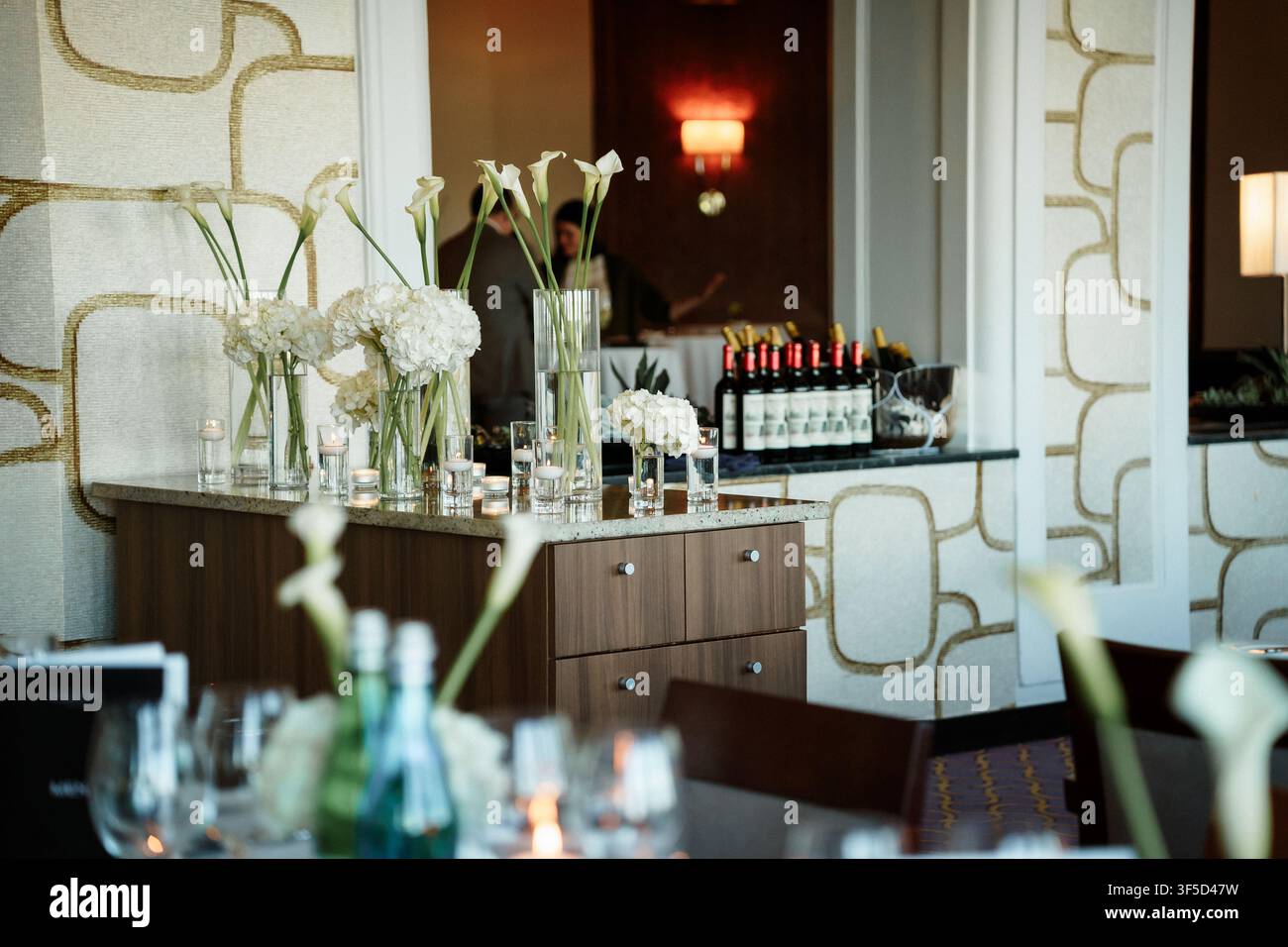 Allestimento elegante di un bar d'hotel con composizioni floreali bianche e bottiglie di vino, che crea un'atmosfera sofisticata per un evento serale formale o un matrimonio, una celebrazione di lusso, allestimento di un servizio di catering Foto Stock