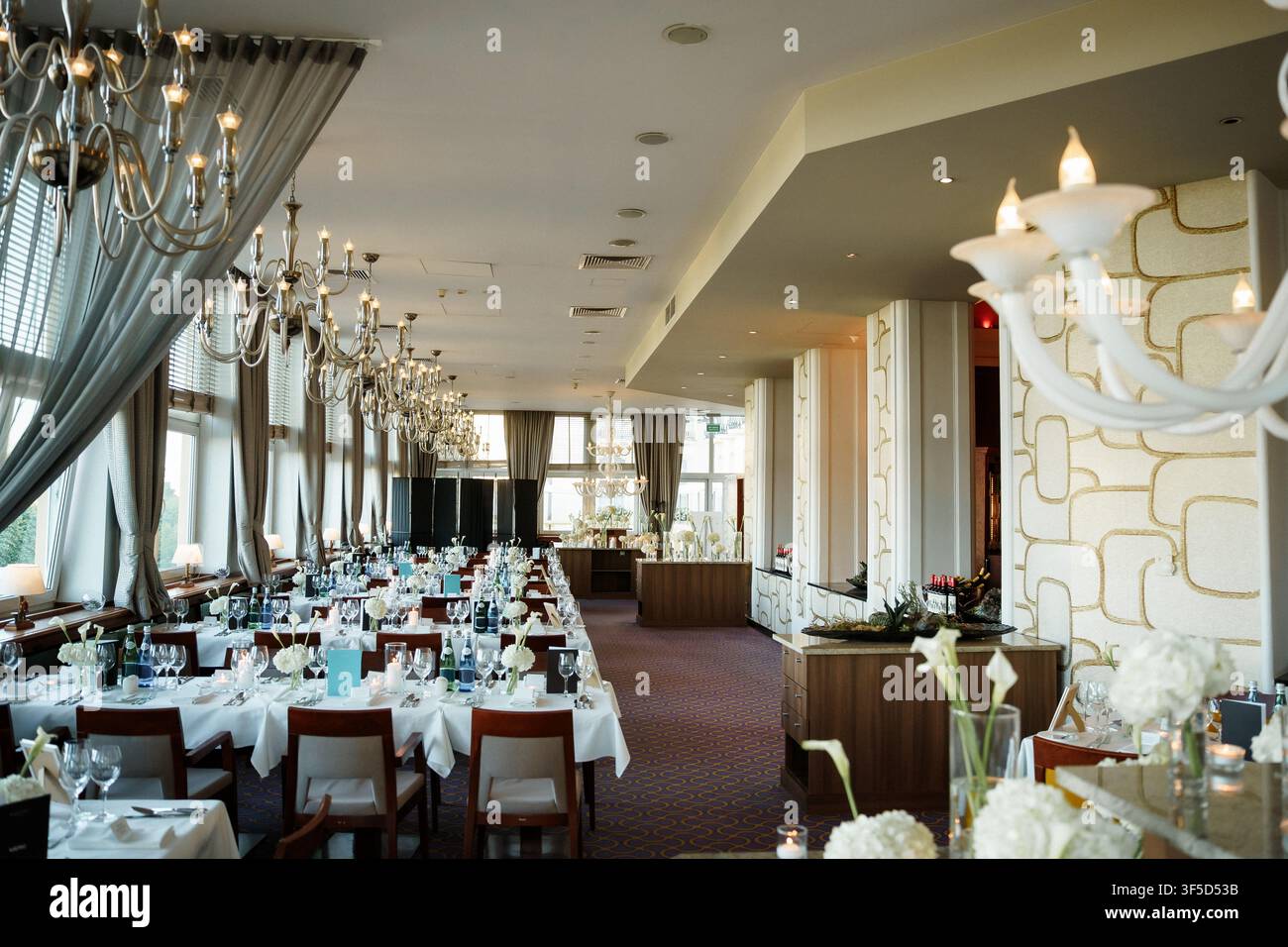 Elegante sala da banchetto allestita per una ricevimento di nozze con lunghi tavoli, lampadari di cristallo e una sofisticata decorazione di lusso Foto Stock