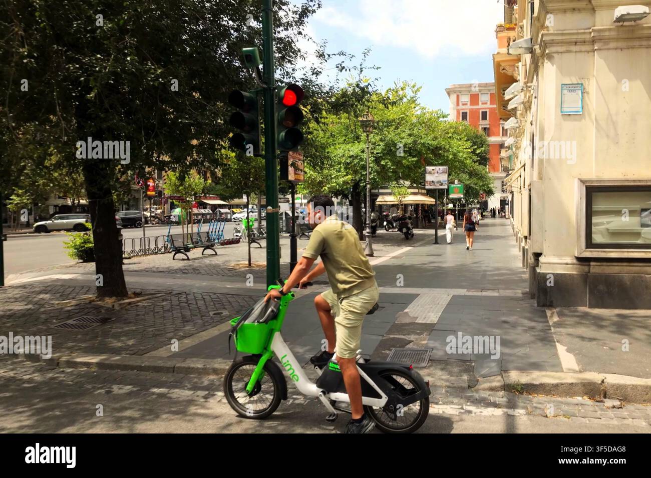 ROMA, ITALIA - 10 LUGLIO 2026: Un uomo guida una bicicletta elettrica condivisa verde lungo una strada cittadina a Roma. Foto Stock