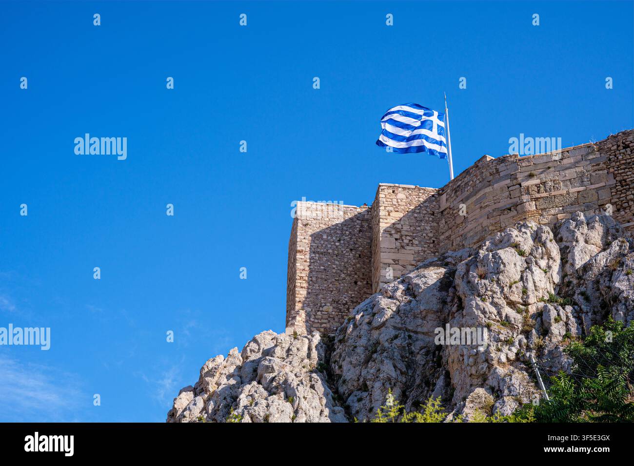 Bandiera greca che sventola dalle mura della fortezza di pietra dell'Acropoli ad Atene, Atene, Grecia Foto Stock