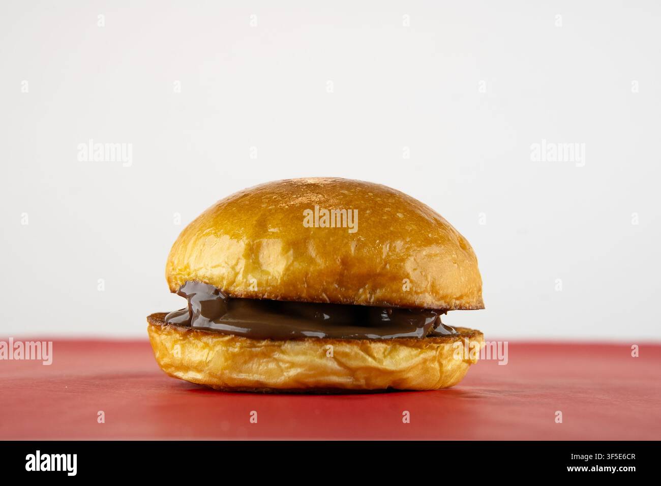 Panino dolce con ricca crema al cioccolato su superficie rossa, dessert indulgente Foto Stock