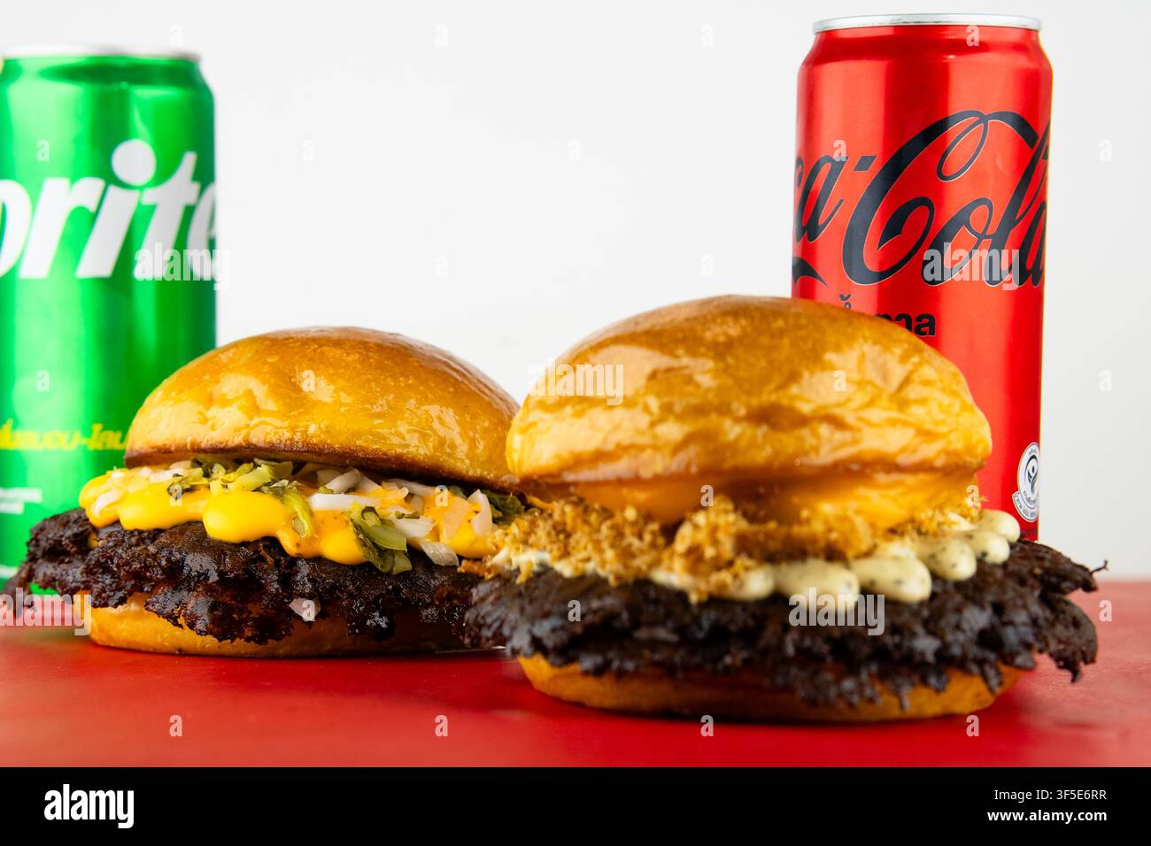 Hamburger schiacciati e lattine di bibite su superficie rossa, raffiguranti un pasto indulgente Foto Stock