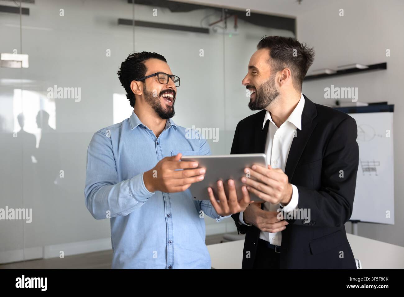 Colleghi multietnici felici che ridono e rivedono i contenuti su un tablet digitale Foto Stock
