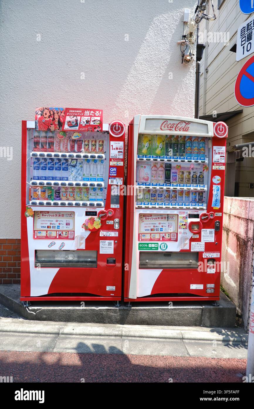 Due distributori automatici rossi di Coca-Cola affiancati contro un muro di edificio su un marciapiede cittadino in Giappone. Foto Stock