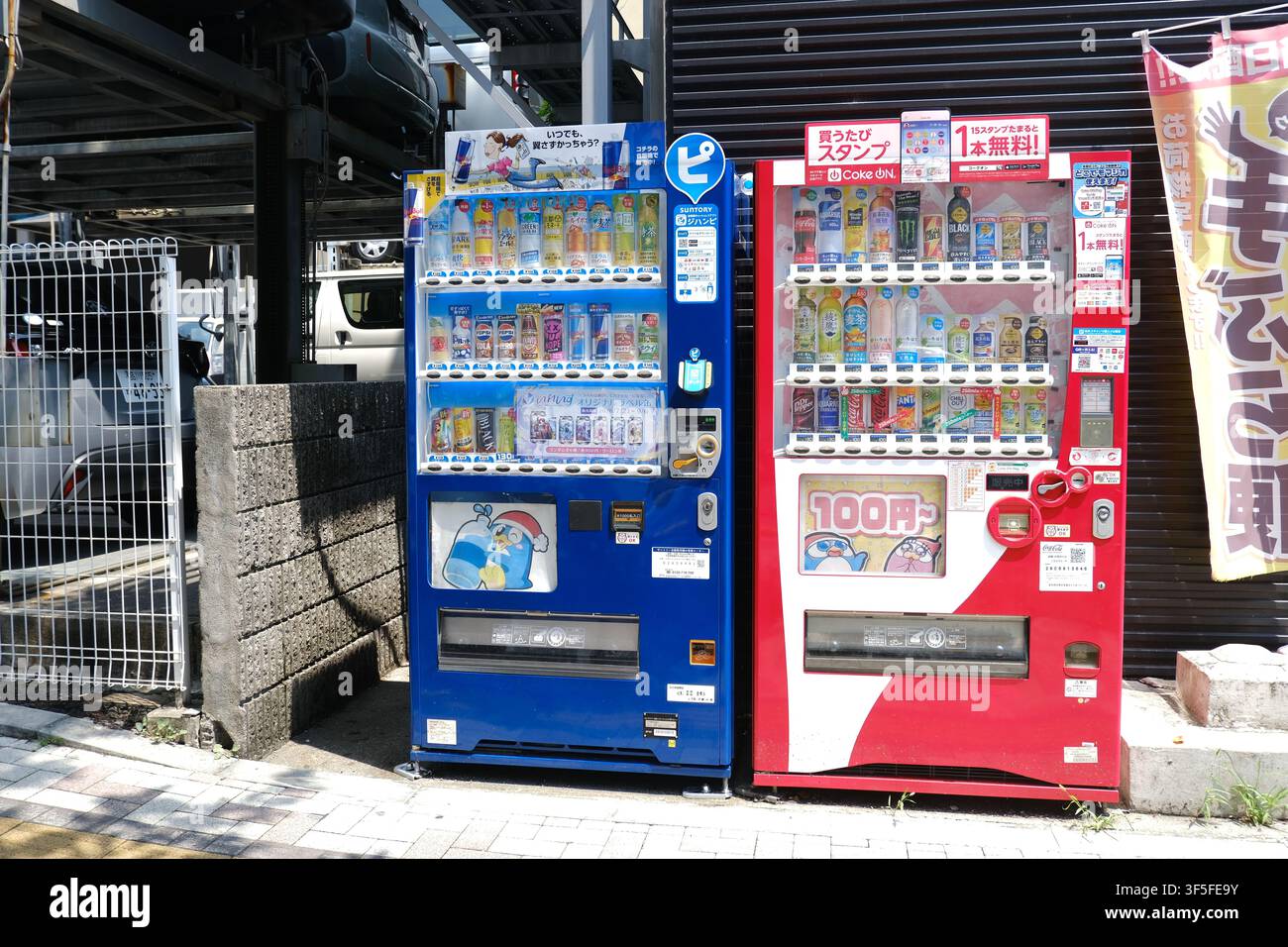 Due distributori automatici di bevande, uno blu e uno rosso Coca-Cola, affiancati su un marciapiede lastricato davanti a un edificio scuro in Giappone. Foto Stock