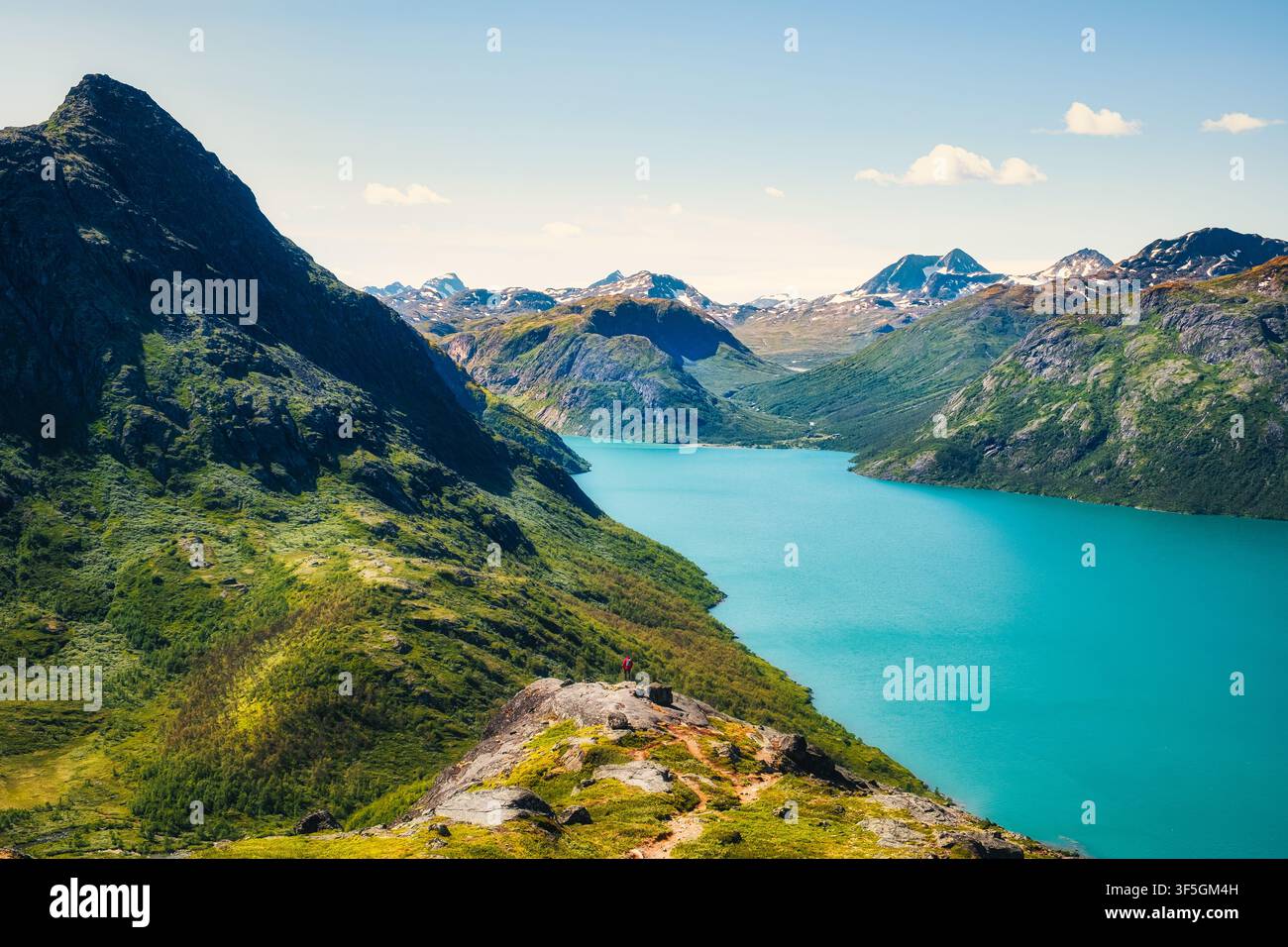 Vista di paesaggio montano di un lago colorato e un escursionista in lontananza, Jotunheimen, Norvegia Foto Stock