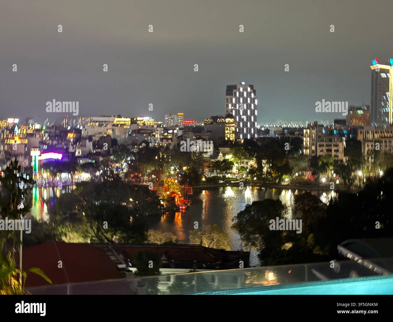 Bar sulla terrazza dell'hotel, vista serale sulla skyline degli storici quartieri antico e francese di Hanoi, e parte del lago circolare Hoàn Kiếm, uno scenario panoramico di 12 h - Immagine stock catturata con smartphone