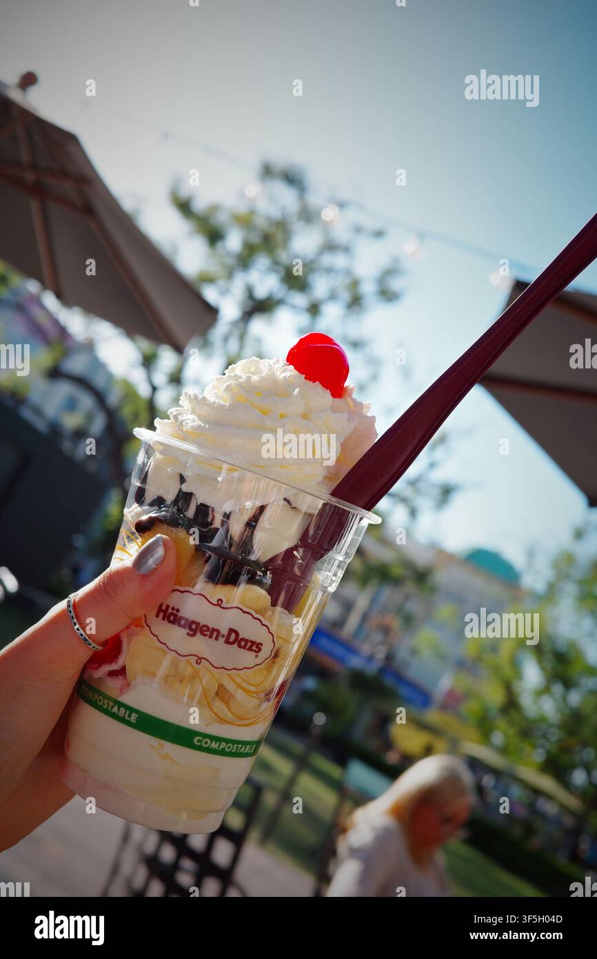 Mano che tiene un sundae di gelato Häagen-Dazs con panna montata e ciliegia all'aperto Foto Stock