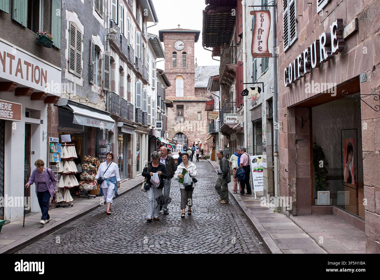 Turisti che camminano lungo la strada acciottolata Rue d'Espagne verso la Chiesa di Notre Dame, Saint-Jean-Pied-de-Port, Paesi Baschi, Francia. Foto Stock