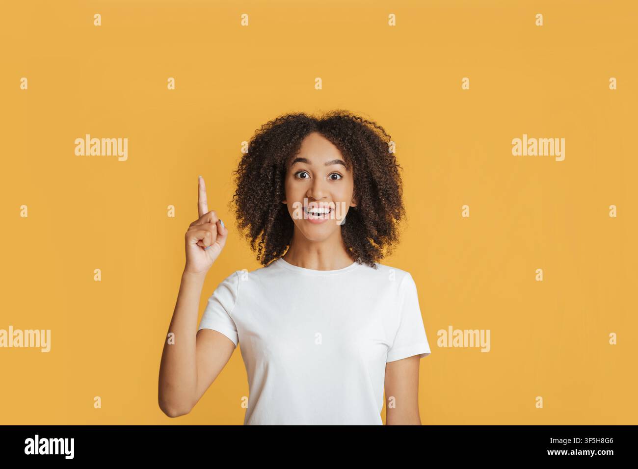 Ottima idea o buona offerta. Sorridente giovane afroamericana eccitata in una maglietta bianca punta il dito verso l'alto Foto Stock