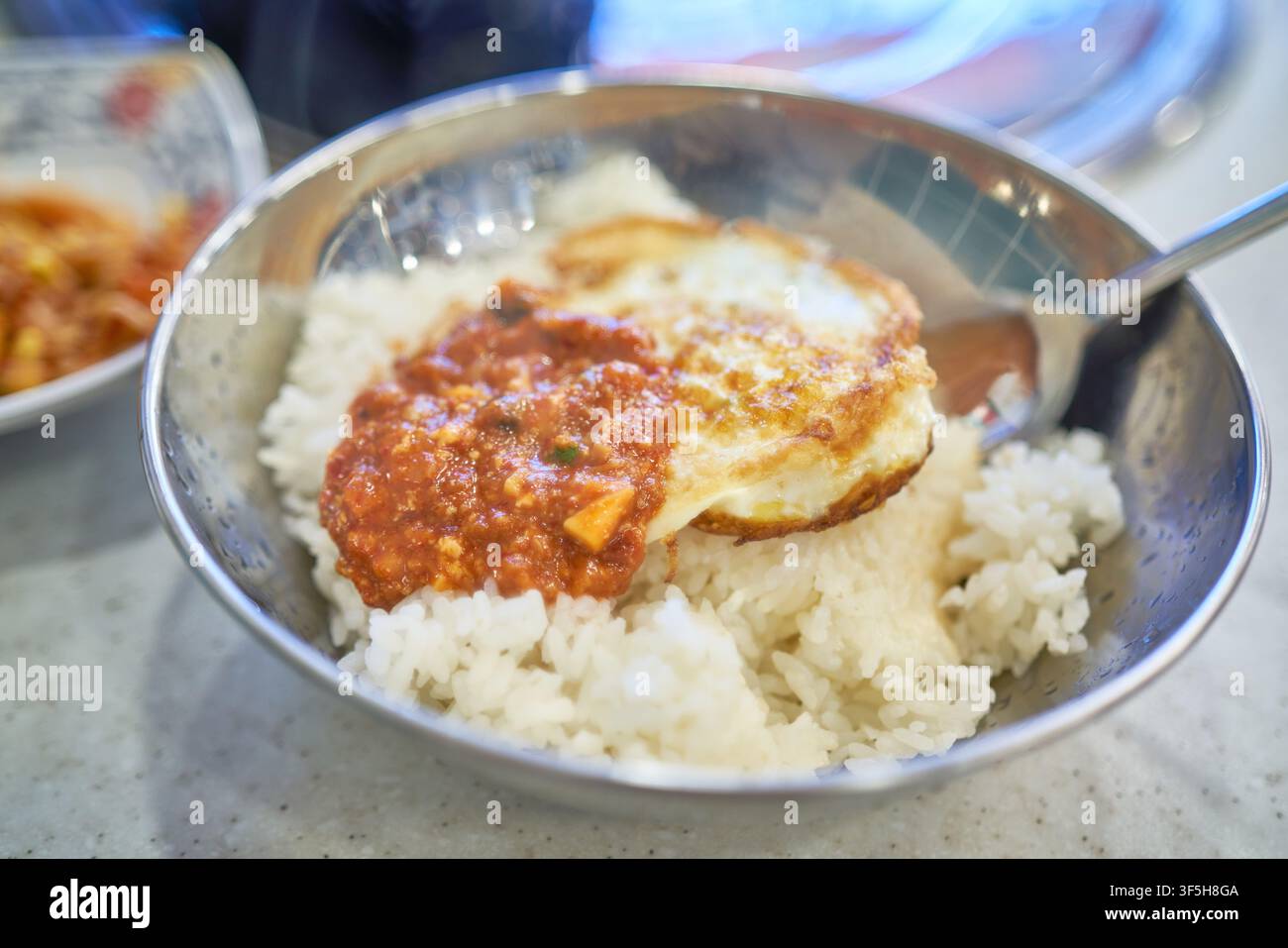 Bibimbap tradizionale coreano makjang guarnito con un uovo fritto e pasta di soia speziata in una ciotola di acciaio inossidabile. Foto Stock