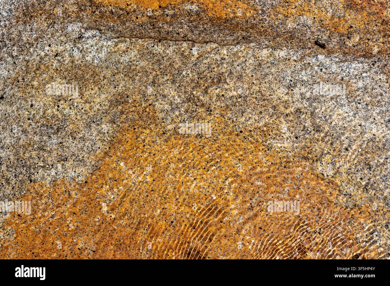 L'acqua crea increspature su una superficie rocciosa ruvida in un ambiente naturale. I colori si mescolano dolcemente, mostrando diversi minerali e stili della pietra. Th Foto Stock