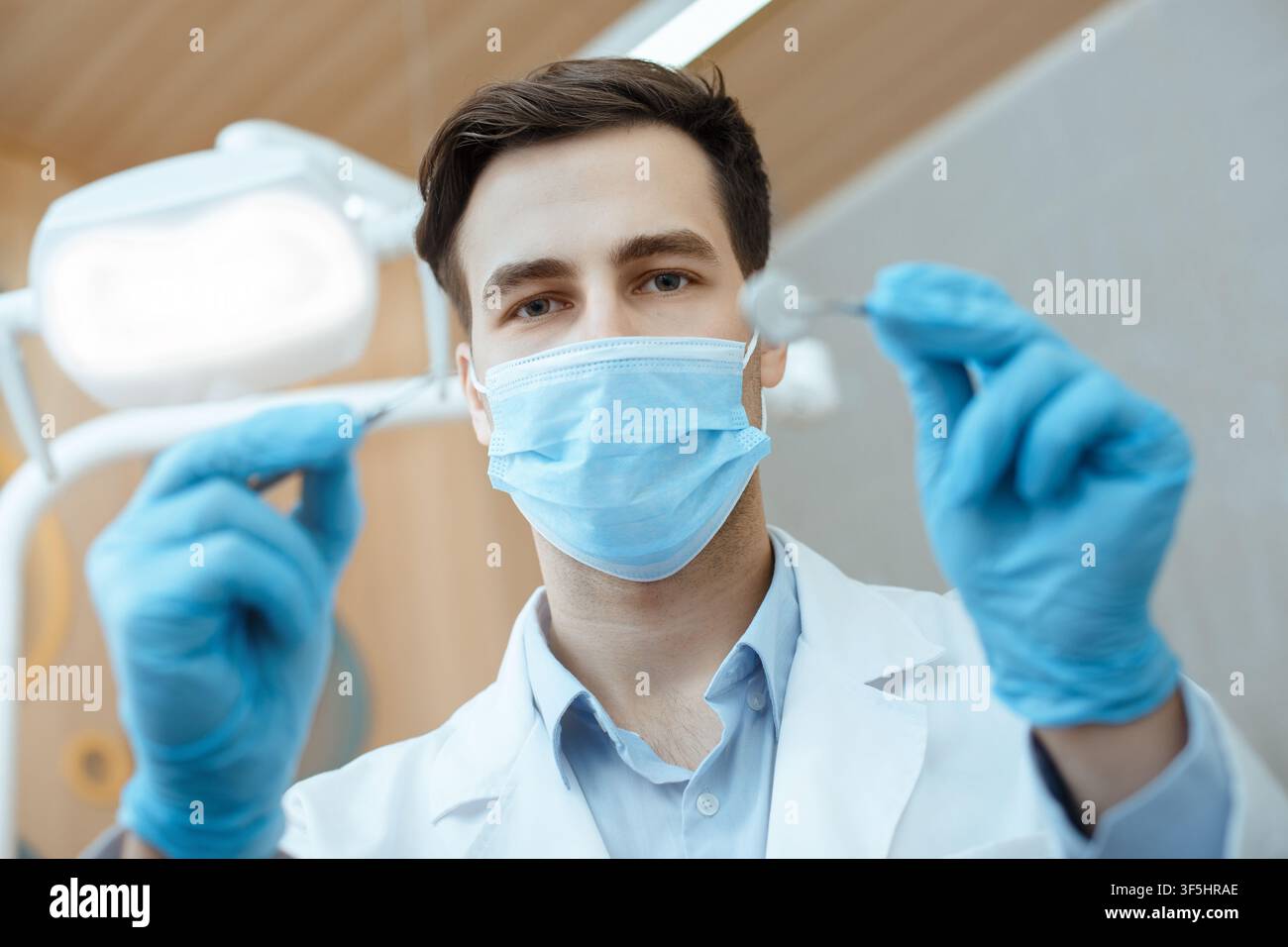 Dentista maschile professionale in camice bianco, maschera protettiva e guanti tenere strumenti dentali e iniziare il lavoro Foto Stock