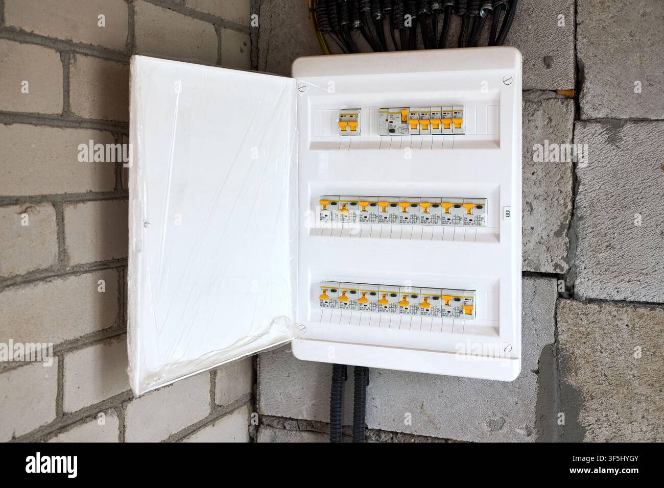 Tablero di distribuzione elettrica aperto su muro di mattoni in cemento con interruttori a tempo, cavi e tubi per l'alimentazione elettrica domestica durante la costruzione e la ristrutturazione Foto Stock