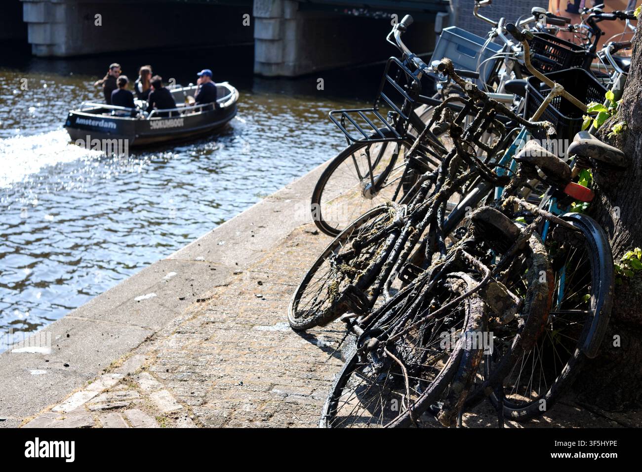 Amsterdam, Olanda Settentrionale, Paesi Bassi - 04 18 2025: Biciclette abbandonate e altre parcheggiate sul molo di un canale di Amsterdam. Foto Stock
