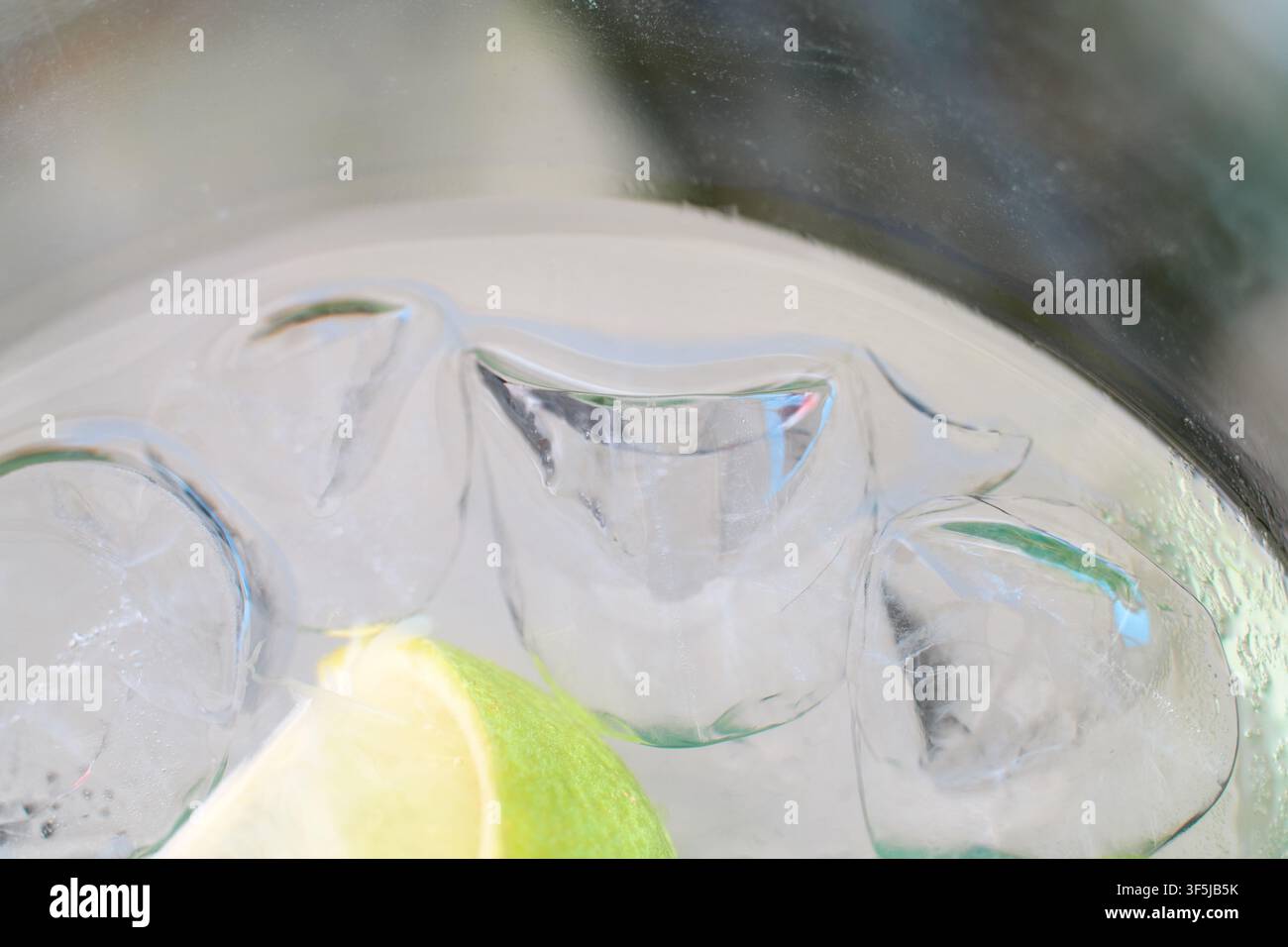 Primo piano di cubetti di ghiaccio cristallini che galleggiano con una vivace fetta di lime all'interno di un bicchiere da cocktail rinfrescante pieno di bevanda gassata. Foto Stock